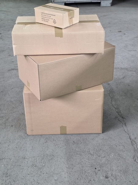 Drei Kartons in verschiedenen Größen, übereinander gestapelt, auf einem grauen Untergrund.