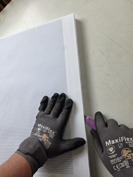 Eine Hand mit Arbeitshandschuhen schneidet ein Blatt Papier mit einem Marker.