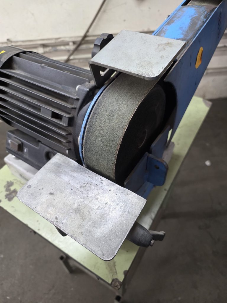 Schleifmaschine mit Motor und zwei Schleifflächen auf grünem Tisch.