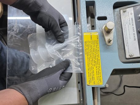 Eine Person mit Handschuhen schneidet eine transparente Folie an einer Maschine.