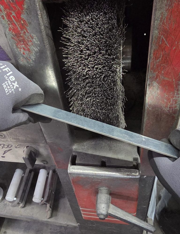 Bürste und Metallplatte in einer Werkstatt, Werkzeug und Staub sichtbar.