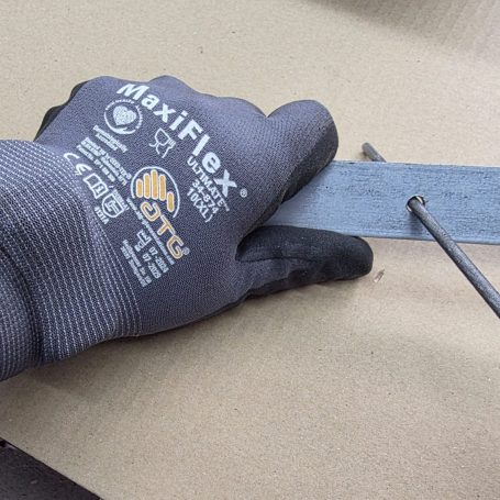 Eine Hand mit einem grauen Arbeitshandschuh hält ein Metallmaßband und einen Schraubendreher.