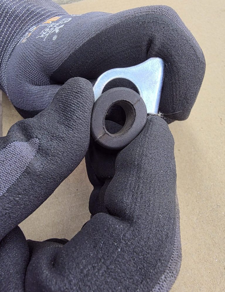 Eine Hand in Handschuhen hält eine metallene Zuglasche und eine Gummimutter.